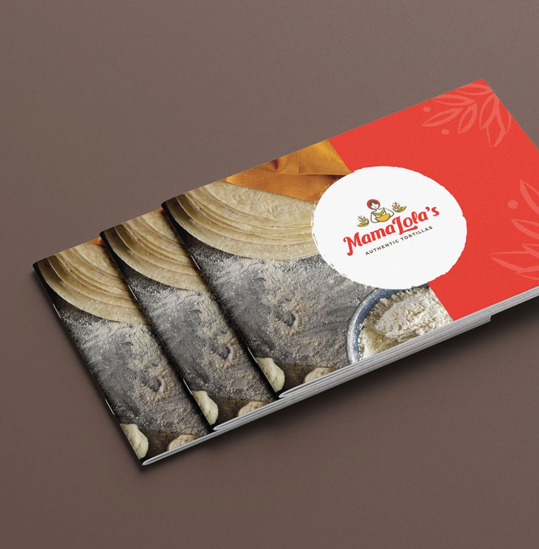 Three Mama Lola's tortilla packages are stacked, showing dough, flour, and the red Mama Lola's label on a brown surface
